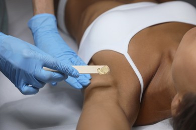 Young woman undergoing hair removal procedure of armpits with sugaring paste in salon, closeup