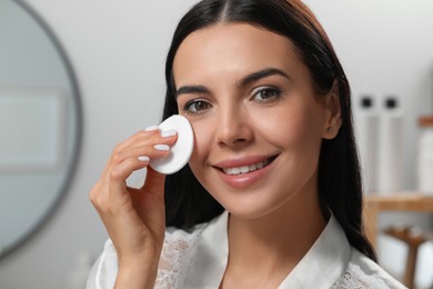 Photo of Young woman using cotton pad with micellar water indoors