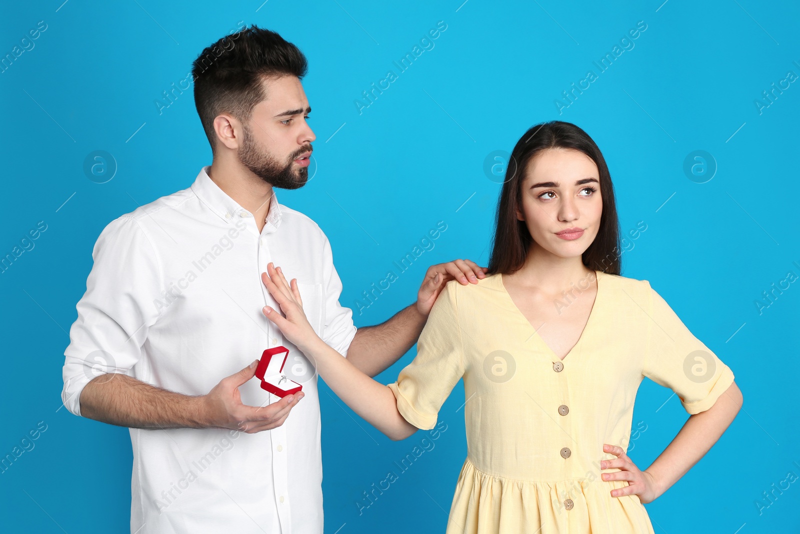 Photo of Young woman rejecting engagement ring from boyfriend on blue background