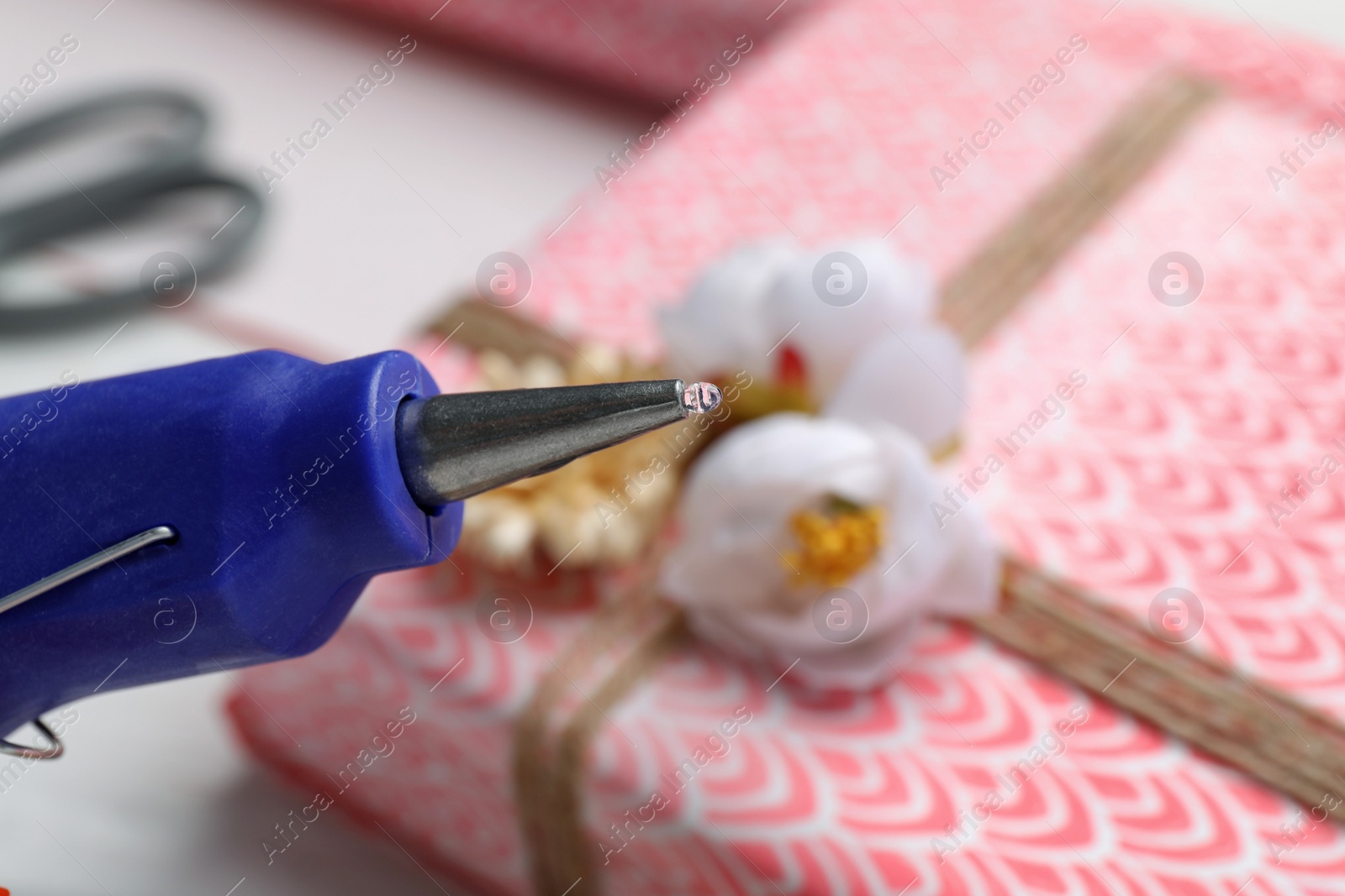 Photo of Hot glue gun and gift on table, closeup