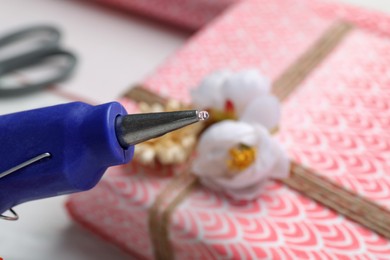 Photo of Hot glue gun and gift on table, closeup