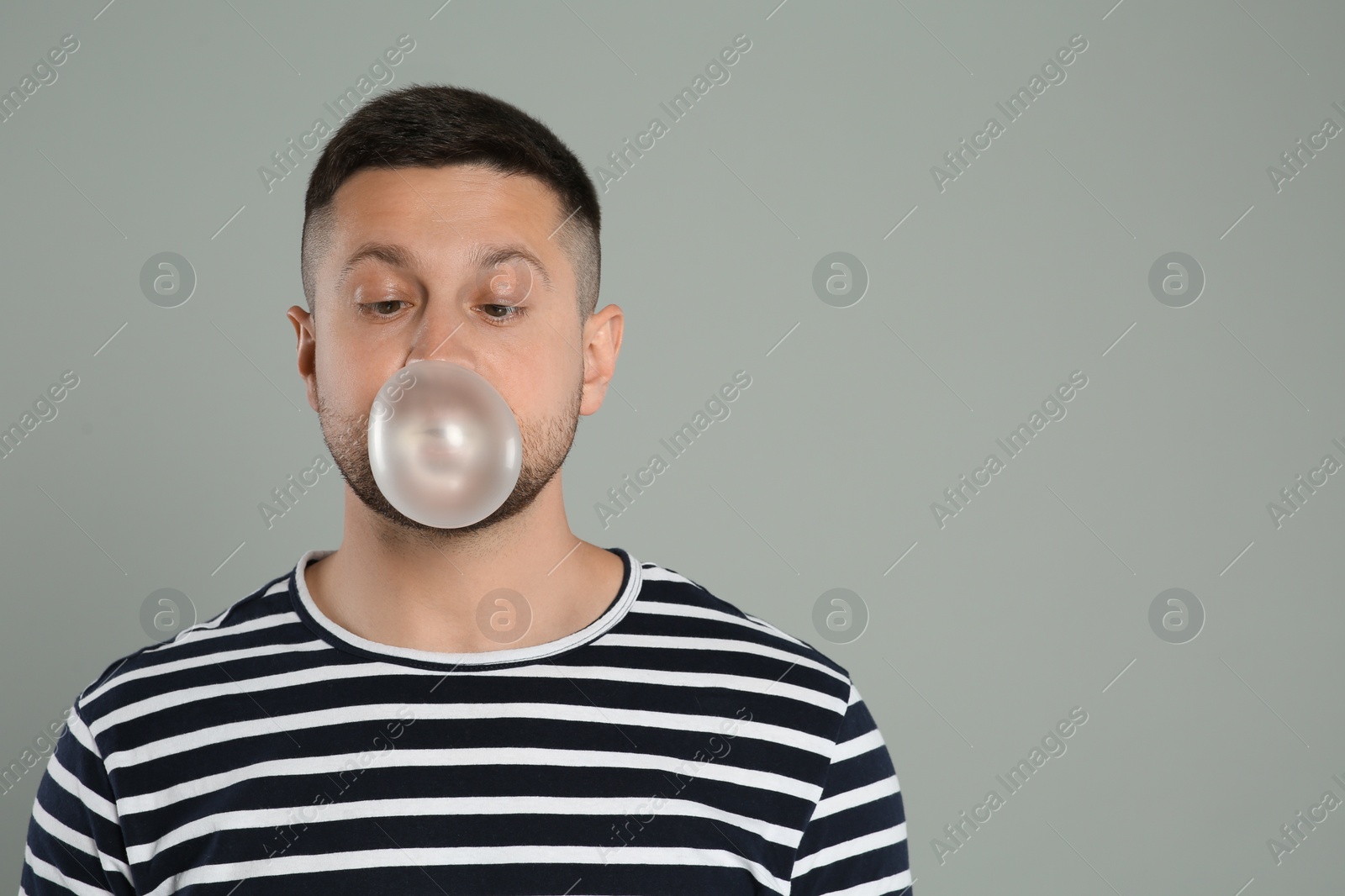Photo of Handsome man blowing bubble gum on light grey background, space for text