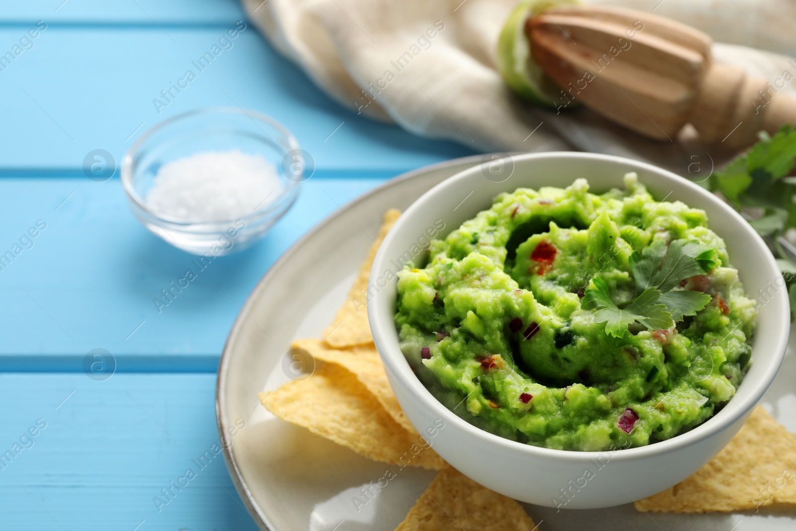Photo of Delicious guacamole served with nachos chips on light blue wooden table, space for text