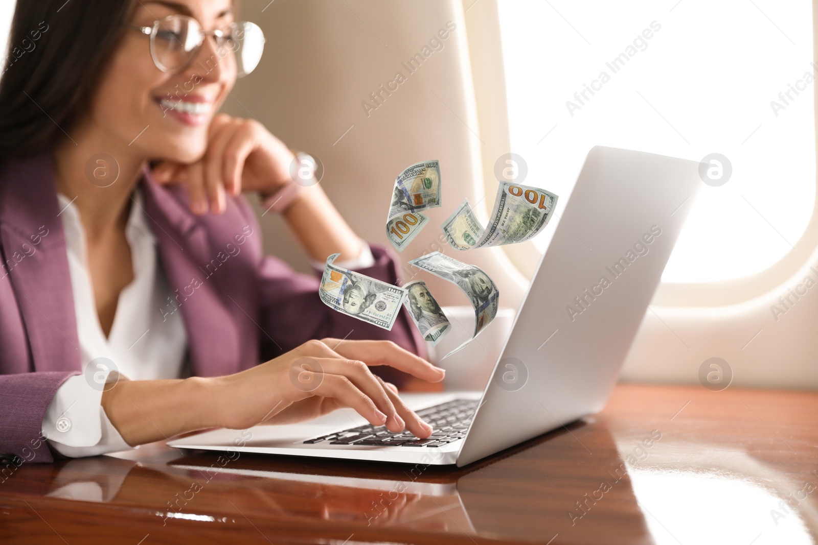 Image of Making money online. Woman using laptop at table and flying dollars