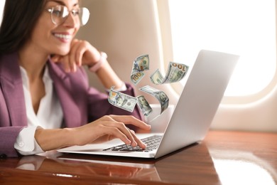 Making money online. Woman using laptop at table and flying dollars