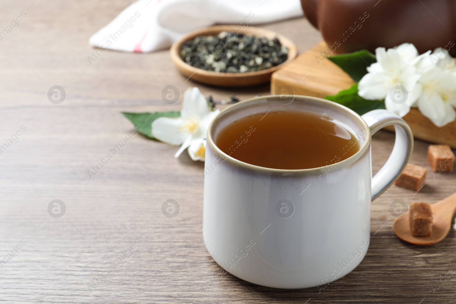 Photo of Cup of tea and fresh jasmine flowers on wooden table. Space for text