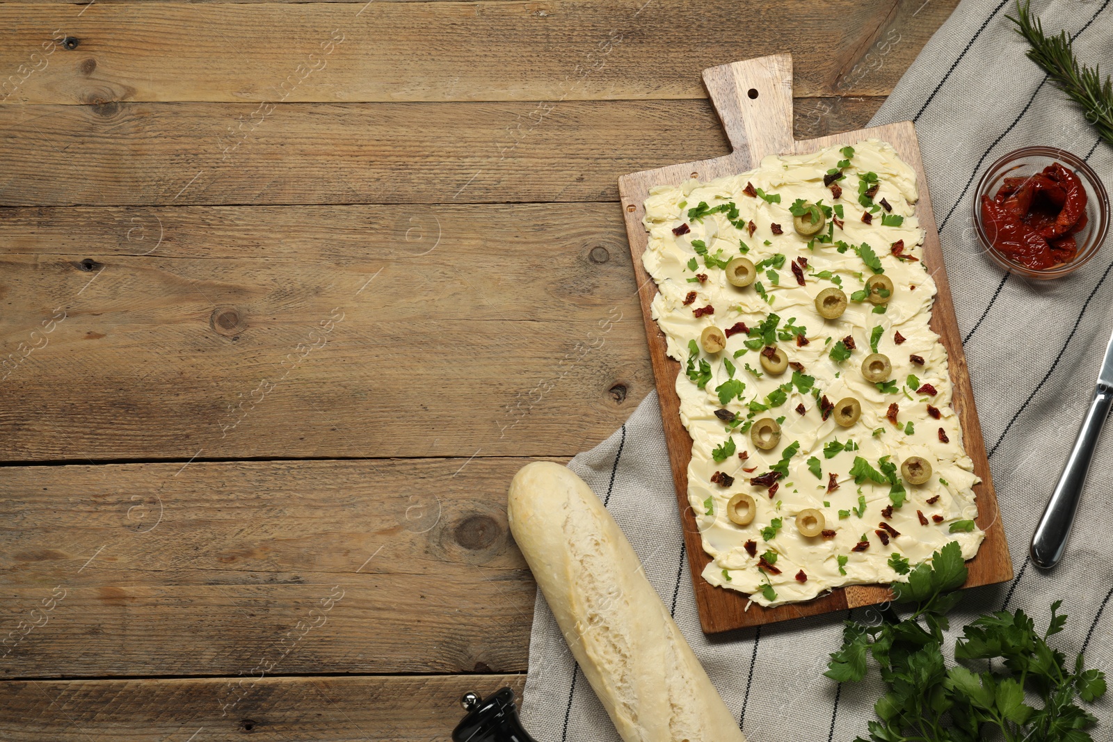 Photo of Fresh butter board with cut olives, sun-dried tomatoes and bread on wooden table, flat lay. Space for text