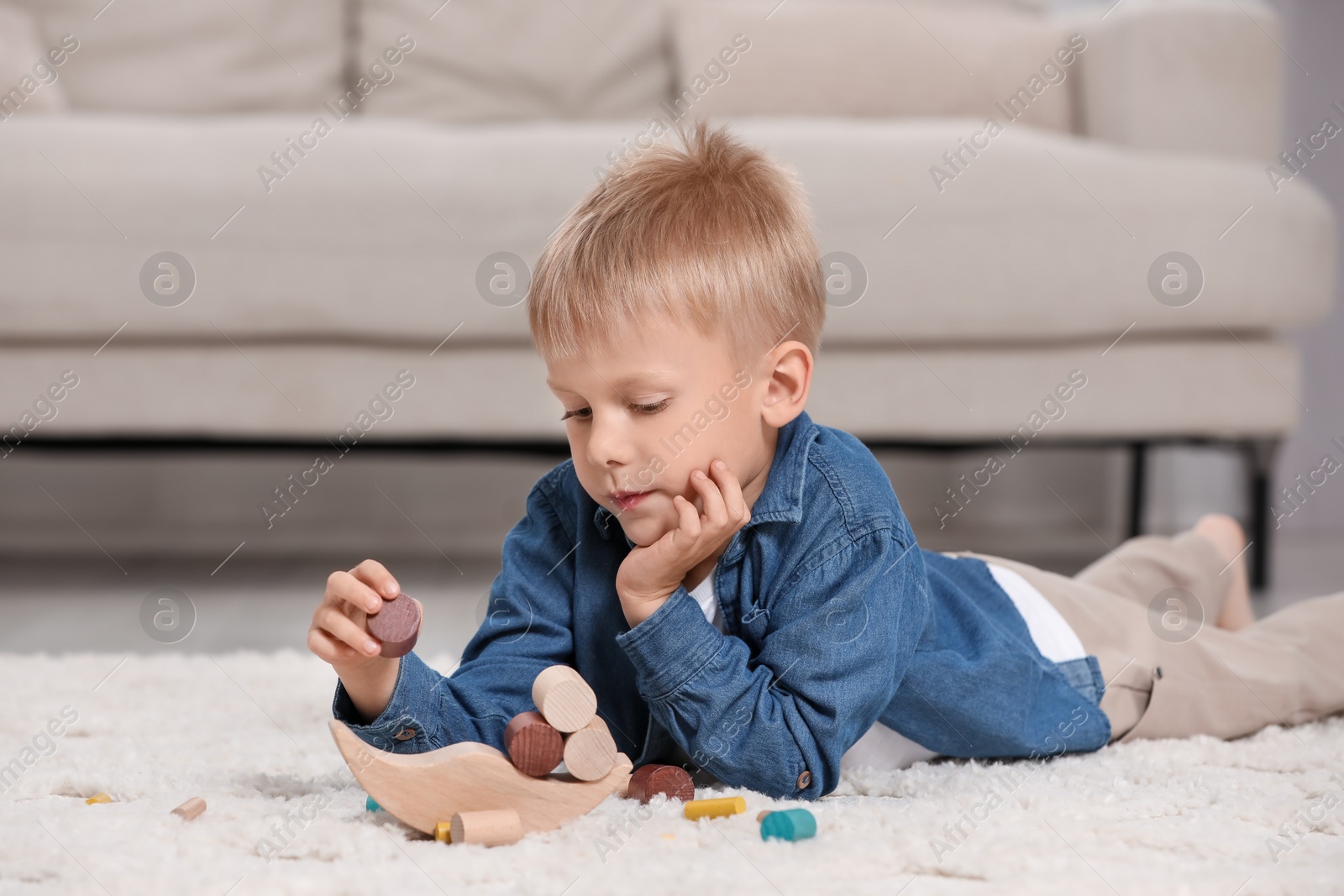 Photo of Cute little boy playing with wooden balance toy on carpet indoors