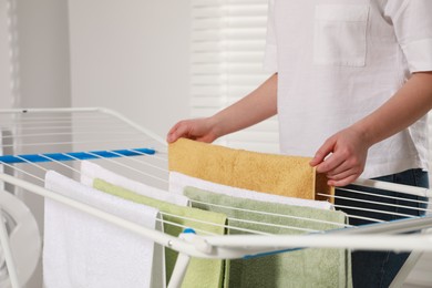 Photo of Woman hanging clean terry towels on drying rack indoors, closeup