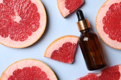 Bottle of cosmetic serum and grapefruit slices on light blue background, flat lay