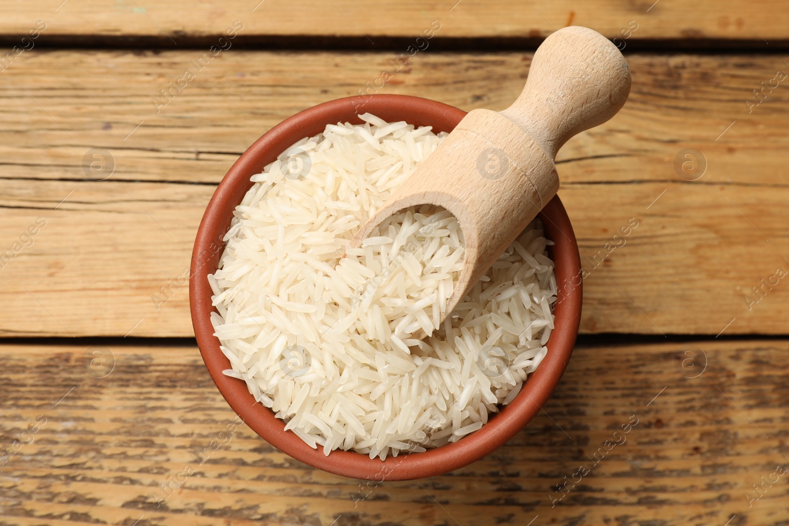 Photo of Raw basmati rice and scoop in bowl on wooden table, top view