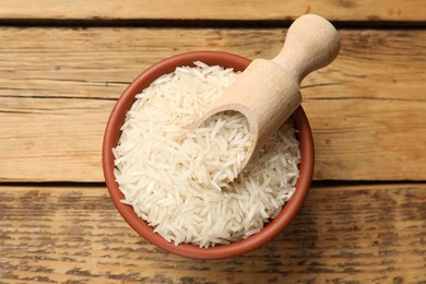 Photo of Raw basmati rice and scoop in bowl on wooden table, top view