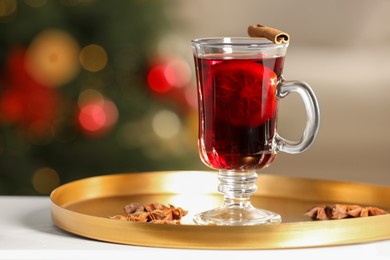 Photo of Delicious mulled wine in glass cup and anise stars on white table against blurred background, closeup. Space for text