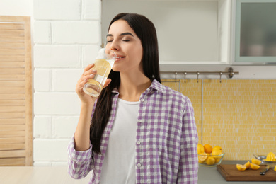 Photo of Beautiful young woman drinking lemon water in kitchen