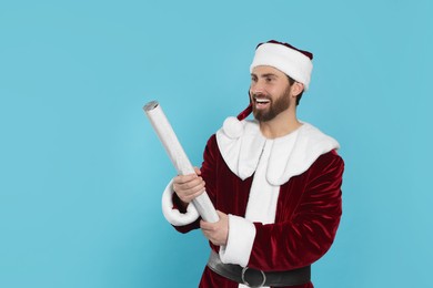 Photo of Happy man in Santa Claus costume with party popper on light blue background. Space for text