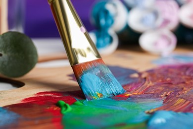 Photo of Mixing colorful paints with brush on wooden artist's palette, closeup