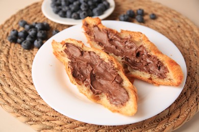 Photo of Tasty croissant with chocolate paste and blueberries on beige background