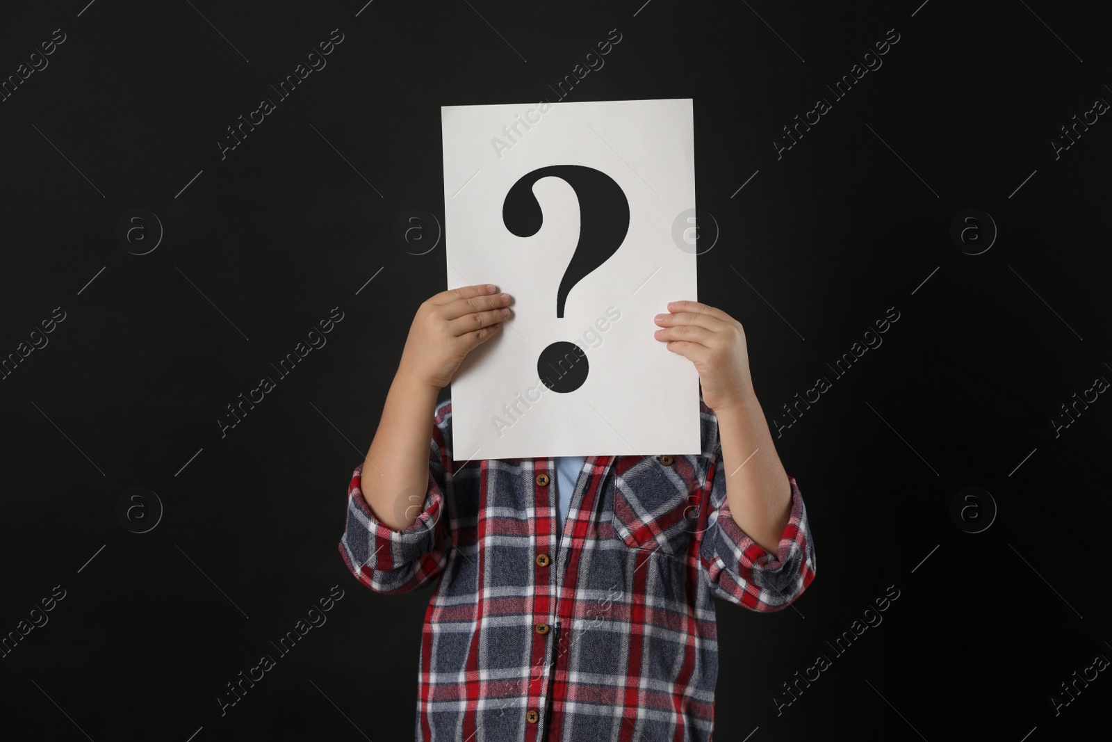 Photo of Child holding sheet of paper with question mark on black background