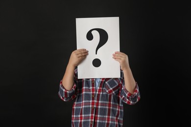 Photo of Child holding sheet of paper with question mark on black background