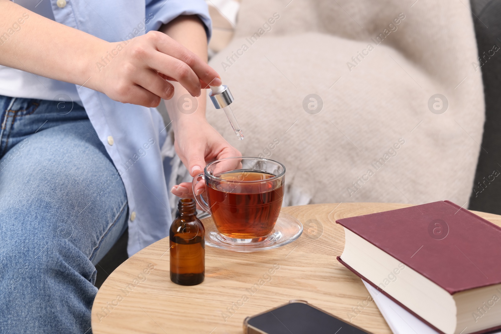 Photo of Woman dripping food supplement into cup of tea at wooden table indoors, closeup