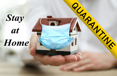 Image of Stay at home during coronavirus quarantine. Man holding house model with medical mask