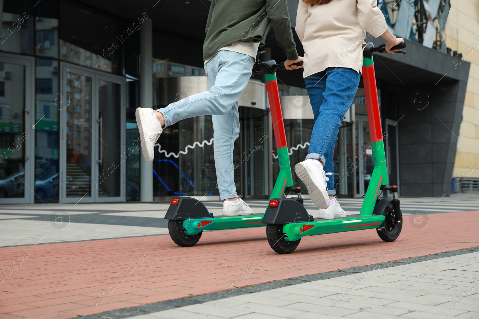 Photo of Couple riding modern electric kick scooters on city street. Space for text