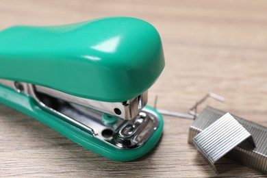 Photo of Turquoise stapler and staples on wooden table, closeup