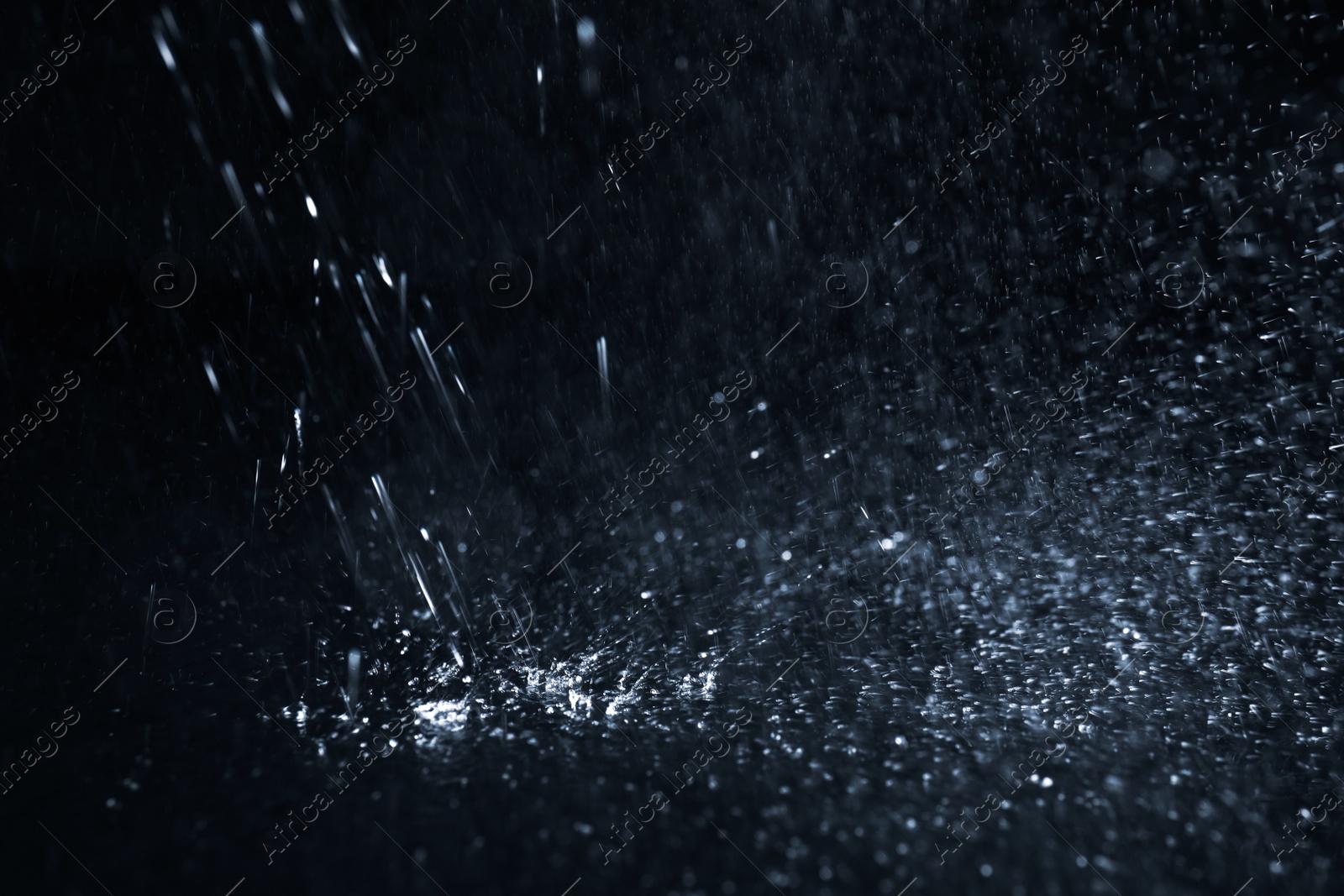 Photo of Heavy rain falling down on ground against dark background, closeup