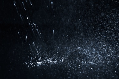 Photo of Heavy rain falling down on ground against dark background, closeup