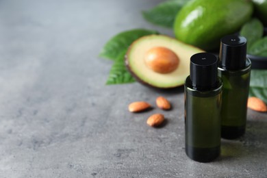 Photo of Bottles of essential oil, avocados and almonds on grey table, space for text