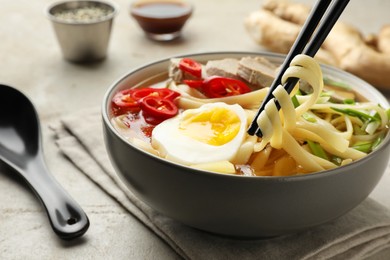 Photo of Eating delicious ramen with chopsticks at light table, closeup. Noodle soup