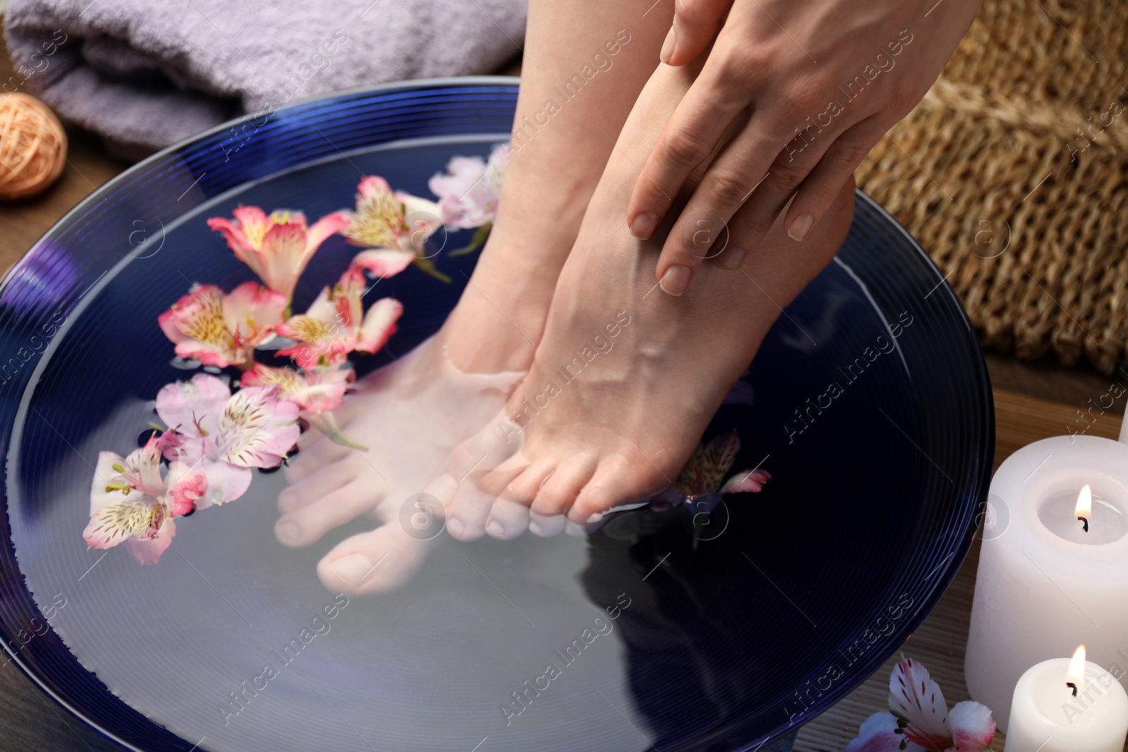 Photo of Woman soaking her feet in bowl with water and flowers on floor, closeup. Spa treatment