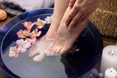 Photo of Woman soaking her feet in bowl with water and flowers on floor, closeup. Spa treatment