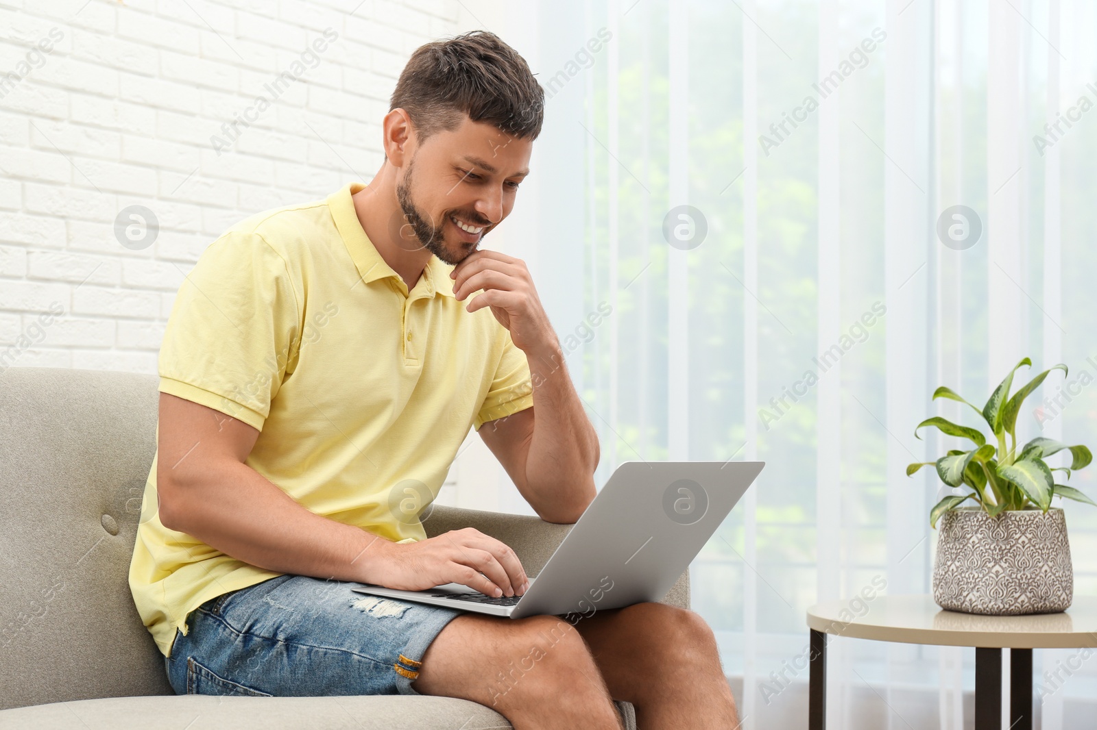 Photo of Happy man using laptop on sofa at home. Internet shopping