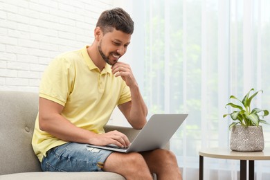 Happy man using laptop on sofa at home. Internet shopping