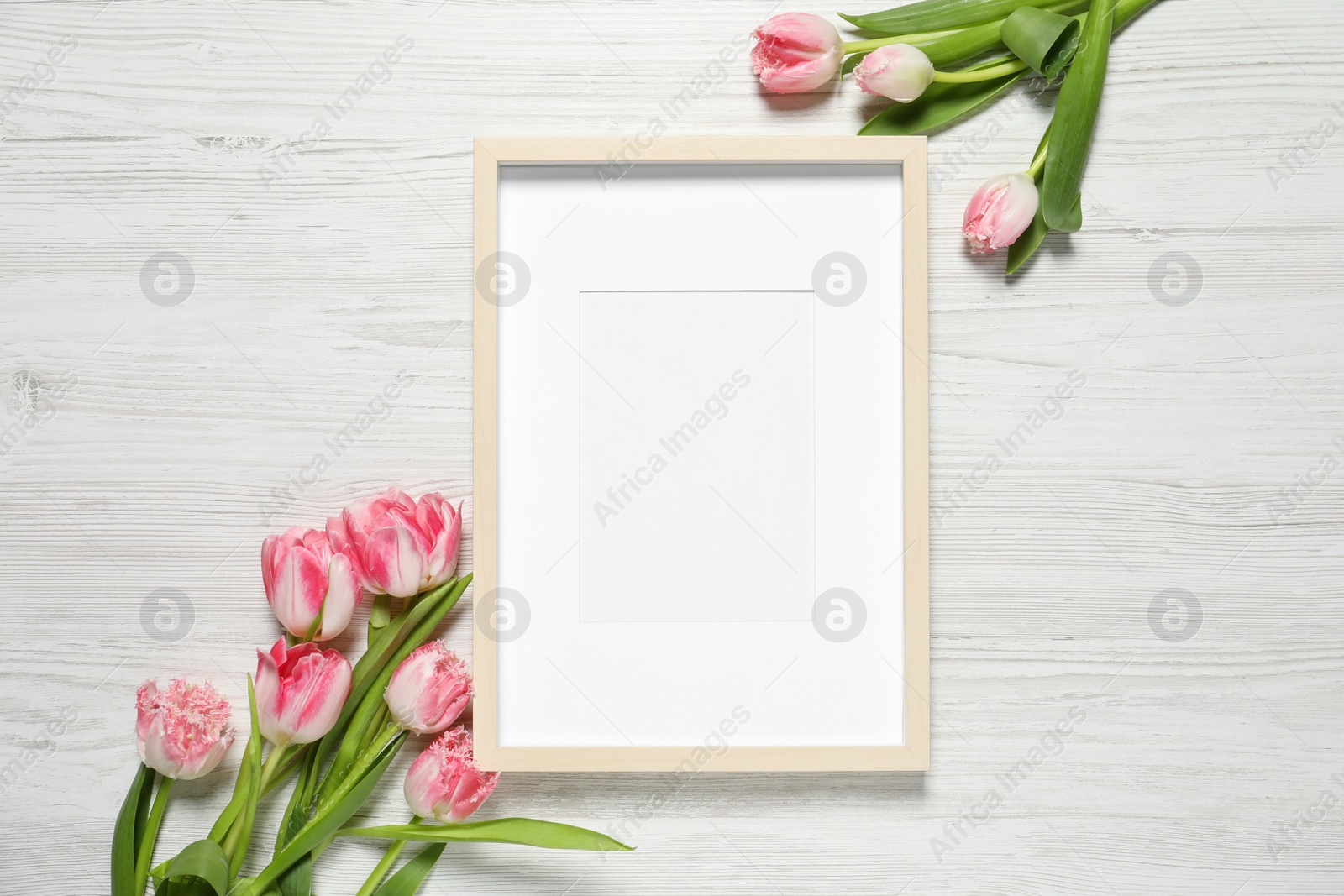 Photo of Empty photo frame and beautiful flowers on white wooden table, flat lay. Space for design