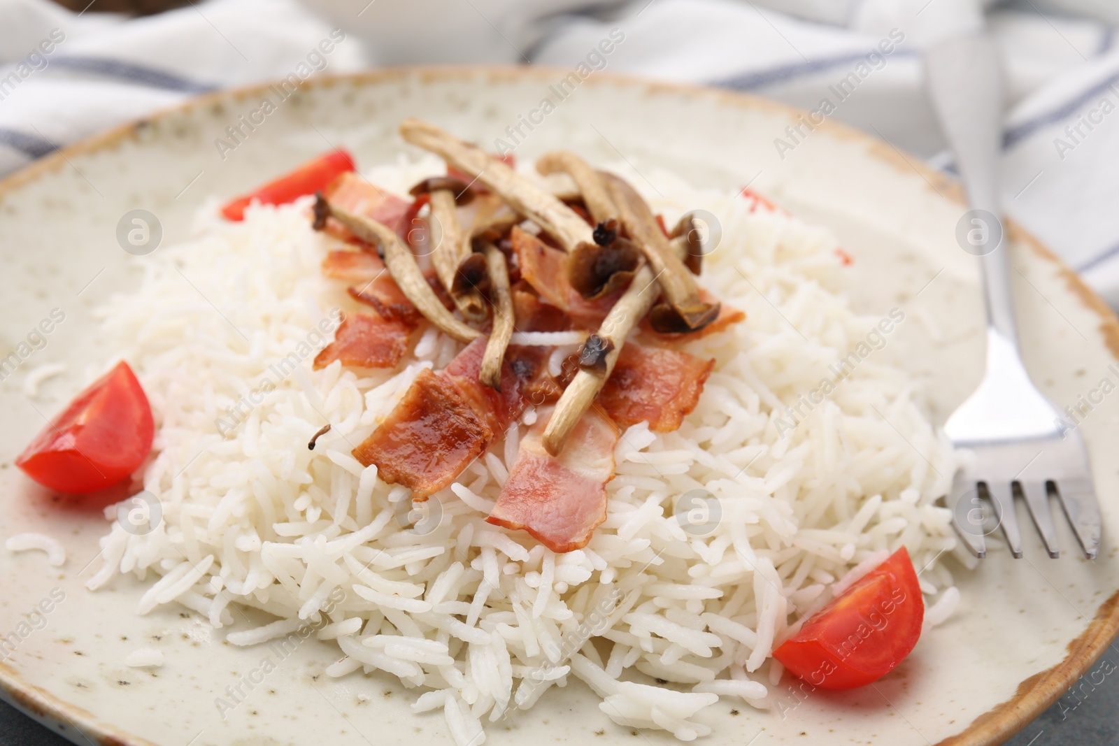 Photo of Delicious rice with bacon, mushrooms and tomatoes served on table, closeup