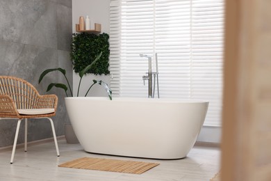 Photo of Green artificial plants and tub near window in bathroom