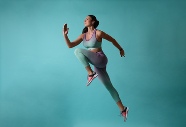 Photo of Athletic young woman running on turquoise background, side view