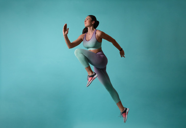 Athletic young woman running on turquoise background, side view