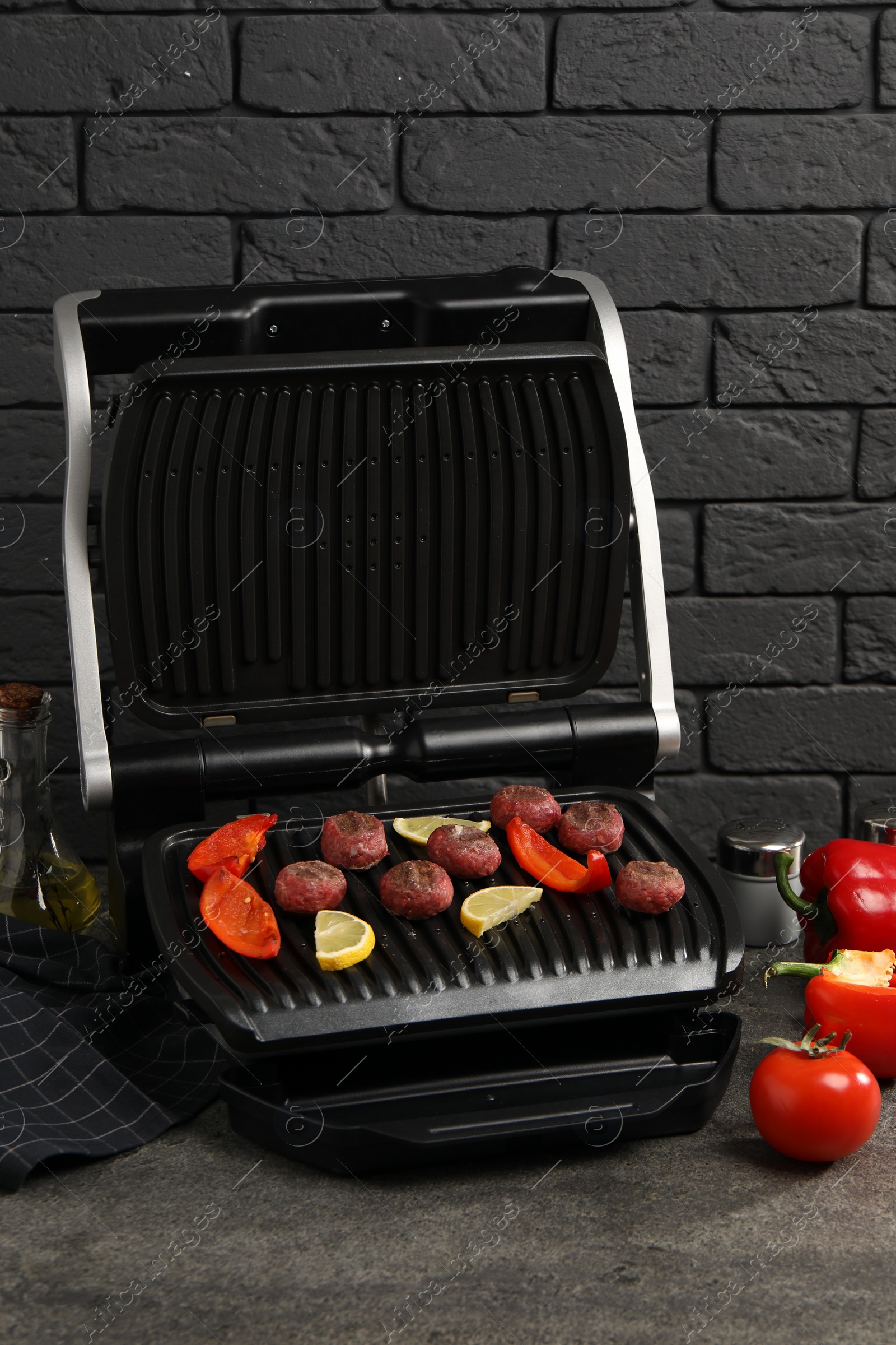 Photo of Electric grill with meat balls, bell peppers and lemon on grey textured table