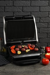 Photo of Electric grill with meat balls, bell peppers and lemon on grey textured table