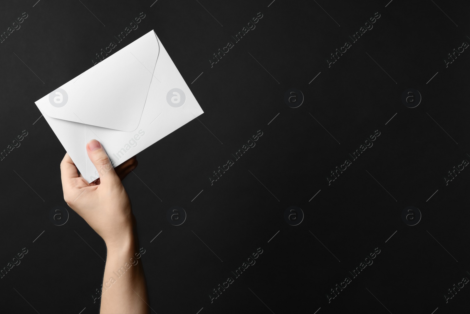 Photo of Woman holding white paper envelope on black background, closeup. Space for text