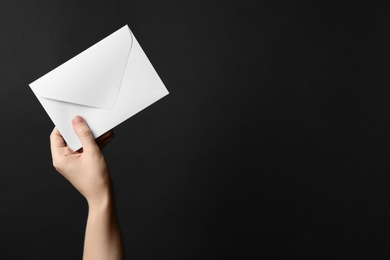 Woman holding white paper envelope on black background, closeup. Space for text