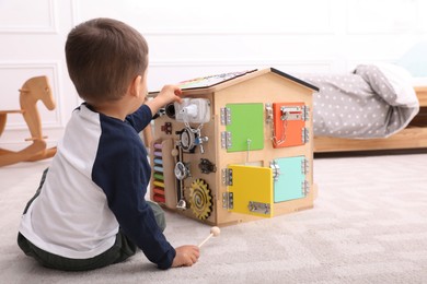 Little boy playing with busy board house on floor at home