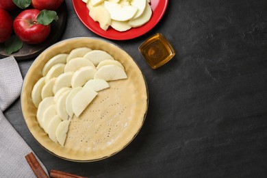 Photo of Flat lay composition with dish of fresh apple slices and raw dough on black table, space for text. Baking pie