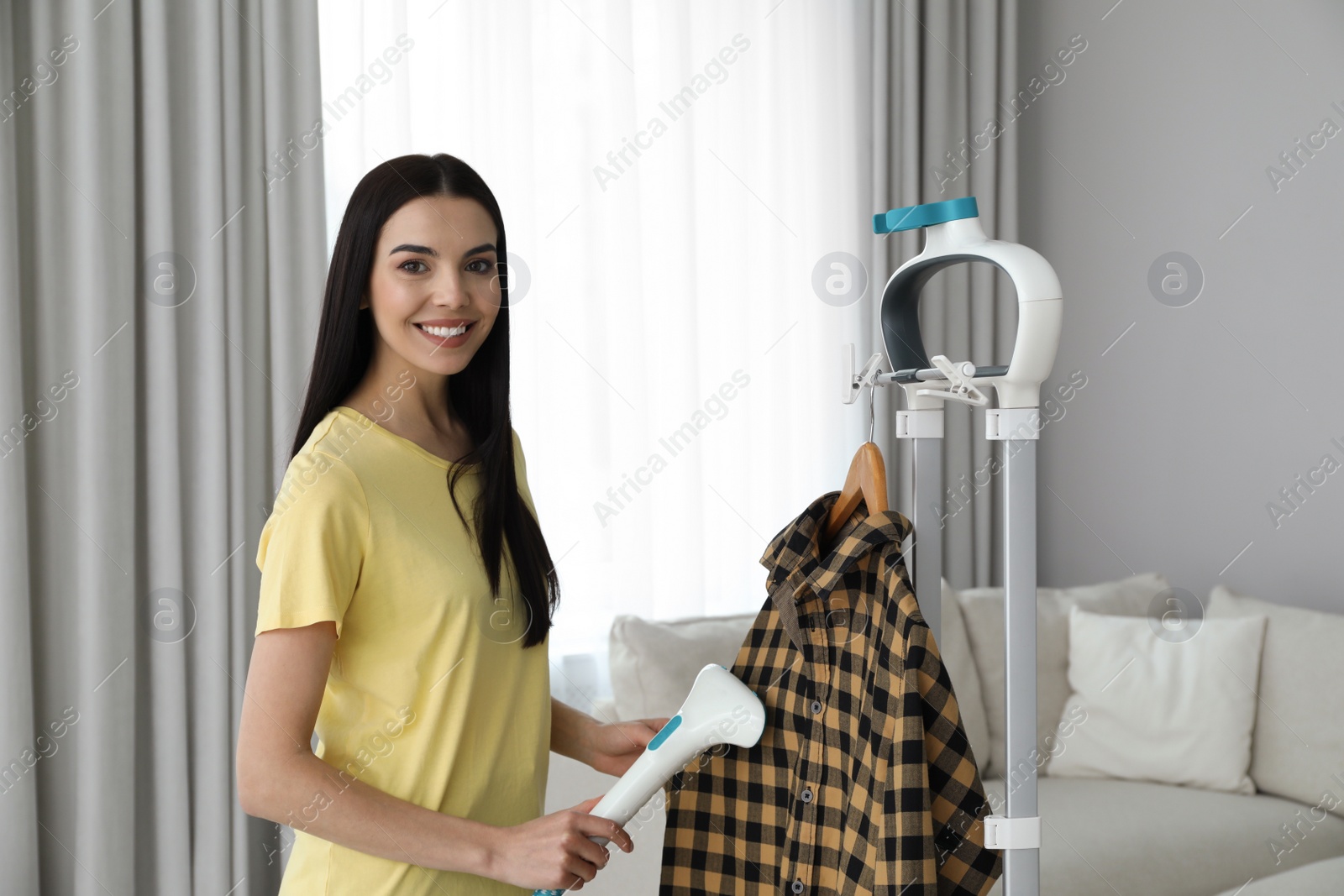 Photo of Woman steaming shirt on hanger at home