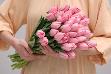 Photo of Woman holding bouquet of pink tulips on light grey background, closeup