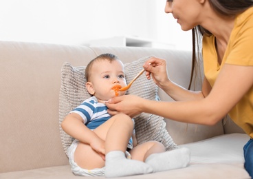 Woman feeding her child on couch indoors. Healthy baby food