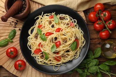 Photo of Delicious pasta with anchovies, tomatoes and basil on wooden table, flat lay